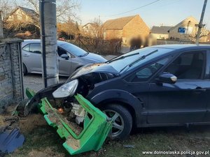 Uszkodzony samochód stoi przy betonowym słupie energetycznym stojącym przy budynku.