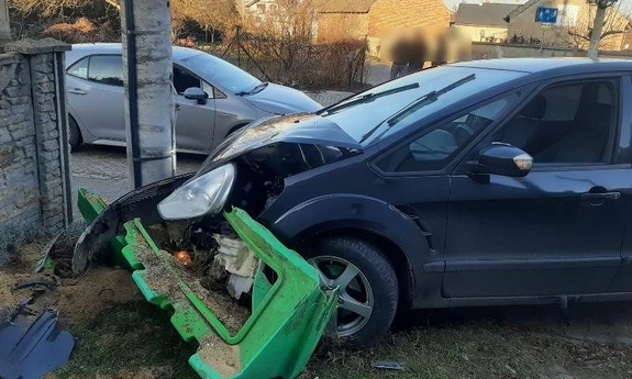 Uszkodzony samochód stoi przy betonowym słupie energetycznym stojącym przy budynku.