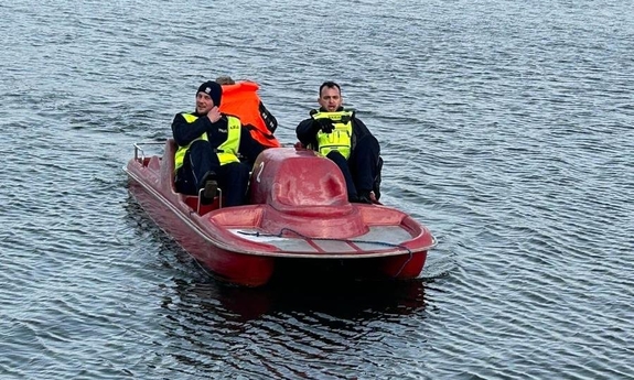 Na zdjęciu umundurowani policjanci na rowerku wodnym ratujący żeglarza w kamizelce ratunkowej, który wpadł do wody.