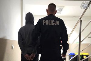 Policjant prowadzi zatrzymanego mężczyznę.