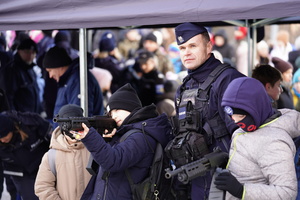 Na zdjęciu umundurowany policjant na stoisku pokazuje dzieciom sprzęt policyjny.