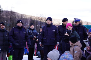 Na zdjęciu umundurowani policjanci na stoku narciarskim, obok policjanta stoi kobieta z dziećmi.