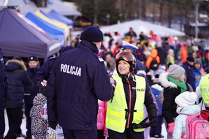 Na zdjęciu policjant i policjantka na stoku narciarskim. W tle rodziny z dziećmi.