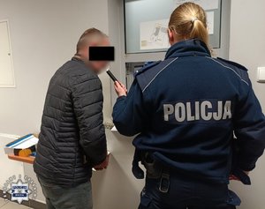 Policjantka i zatrzymany mężczyzna, który dmucha w urządzenie do pomiaru trzeźwości.