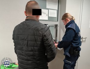 Umundurowana policjantka wypełnia dokumenty. Na pierwszym planie widoczny stojący tyłem zatrzymany mężczyzna.