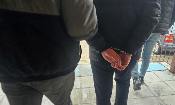 Na zdjęciu dwóch policjantów prowadzi zatrzymanego mężczyznę w kajdankach.