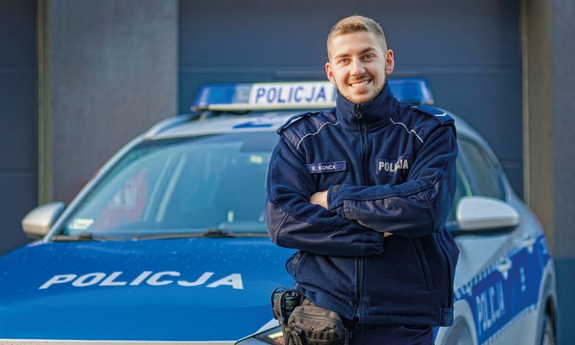 Policjant stoi przy radiowozie policyjnym.