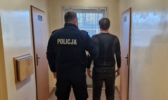 Umundurowany policjant stoi z zatrzymanym mężczyzną.