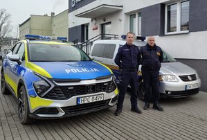 Policjant stoi obok strażnika gminnego, za nimi radiowóz policyjny i pojazd straży gminnej.