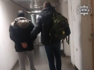 Nieumundurowany policjant prowadzi korytarzem zatrzymanego mężczyznę.