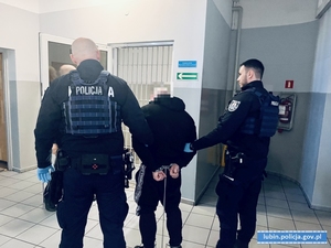 Zatrzymany mężczyzna stojacy z policjantami.