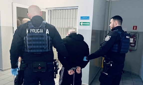 Zatrzymany mężczyzna stojący z policjantami.