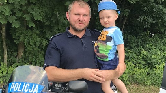 Umundurowany policjant trzyma na ręku dziecko.