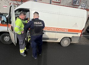 Policjant rozmawiający z pracownikiem gazowni przy charakterystycznym samochodzie pogotowie gazowe.