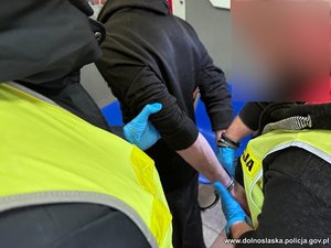 Policjanci zakładają kajdanki na ręce zatrzymanej osoby.