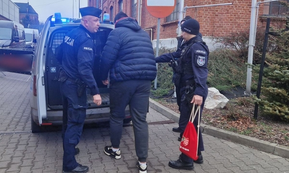 Policjanci umieszczają w oznakowanym radiowozie zatrzymanego wolontariusza.