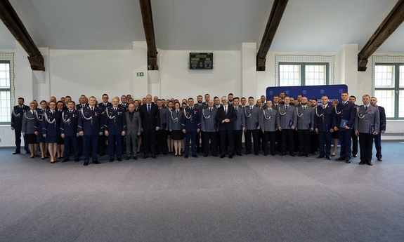 Uczestnicy uroczystości w sali Oddziału Prewencji Policji w Olsztynie pozują do zdjęcia grupowego.