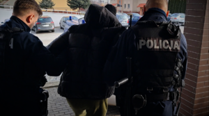 Dwaj umundurowani policjanci prowadzą zatrzymanego mężczyznę.