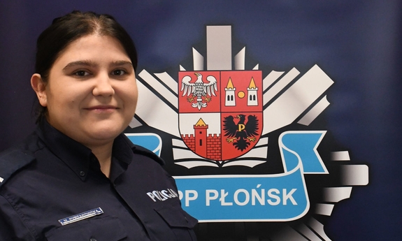 Policjantka stoi na tle banneru z napisem Komenda Powiatowa Policji w Płońsku.