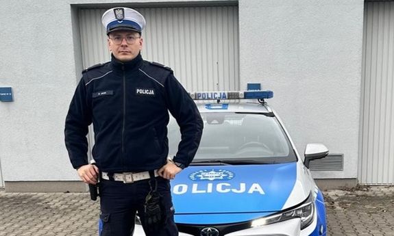 policjant stoi przed radiowozem.