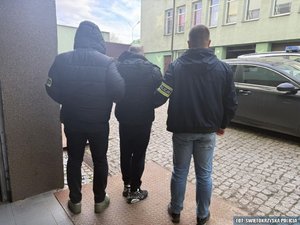 Dwóch policjantów prowadzi zatrzymanego mężczyznę.