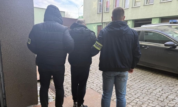 Dwóch policjantów prowadzi zatrzymanego mężczyznę.