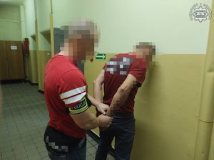 Na zdjęciu policjant z zatrzymanym w kajdankach w pomieszczeniu.