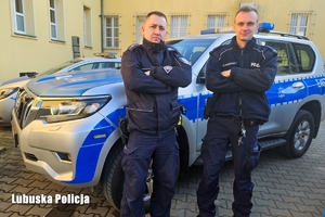 policjanci stoją przed radiowozem.