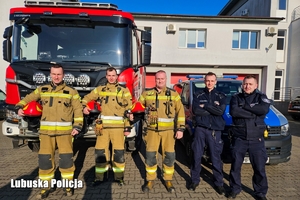 policjanci stoją przed radiowozem, a obok strażacy stoją przed wozem strażackim.