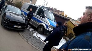 przód samochodu, który stoi obok radiowozu. Obok chodzą policjanci.