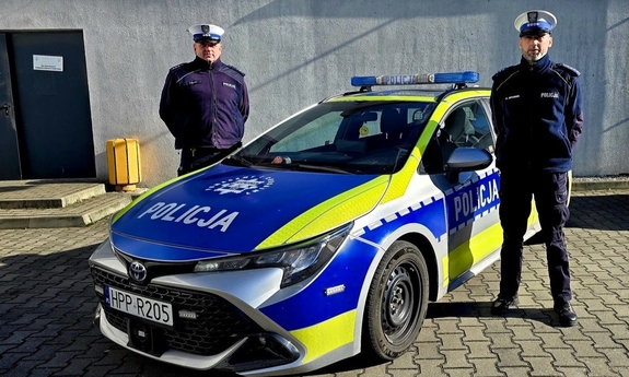 Dwaj policjanci stoją przy radiowozie.