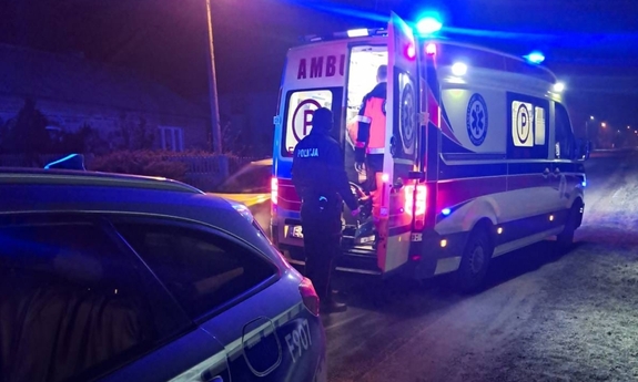 Na miejscu zdarzenia służby ratunkowe, radiowóz policyjny i karetka pogotowia stoją przy drodze, obok karetki stoi policjant.