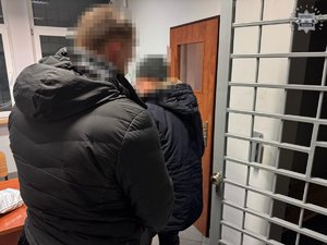 Nieumundurowany policjant trzyma zatrzymanego w pomieszczeniu dla osób zatrzymanych.