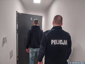 Policjant i zatrzymany mężczyzna w pomieszczeniu stojący tyłem.