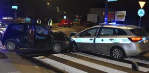 Na drodze uszkodzony radiowóz i samochód osobowy, w tle policjanci i inne osoby.