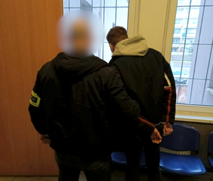 Policjant z zatrzymanym mężczyzną zakutym w kajdanki.