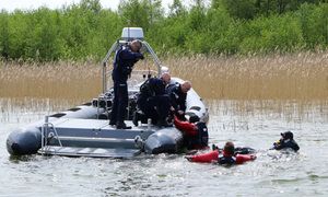 Policjanci na łodzi pontonowej wyciągają z wody mężczyzn.