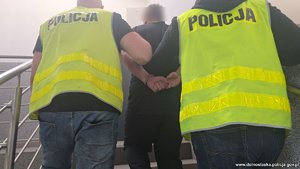 Dwaj policjanci prowadza zatrzymanego w kajdankach.