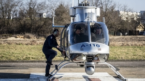 W śmigłowcu policyjnym siedzą piloci obok śmigłowca inny pilot.