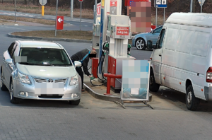 Stacja paliw pojazdy przy dystrybutorach mężczyzna rozlewający paliwo przy dystrybutorze.