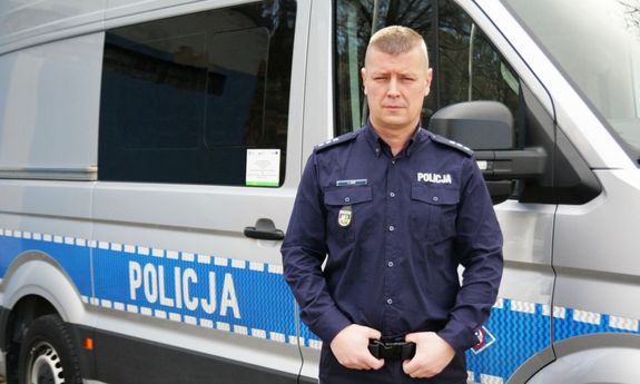 Umundurowany policjant na tle radiowozu.