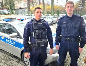 dwóch policjantów stoi przed radiowozem.