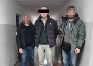 Dwaj policjanci z zatrzymanym mężczyzną w kajdankach.