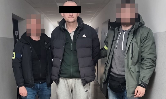 Dwaj policjanci z zatrzymanym mężczyzną w kajdankach.