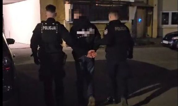 Dwaj umundurowani policjanci prowadzą zatrzymanego.