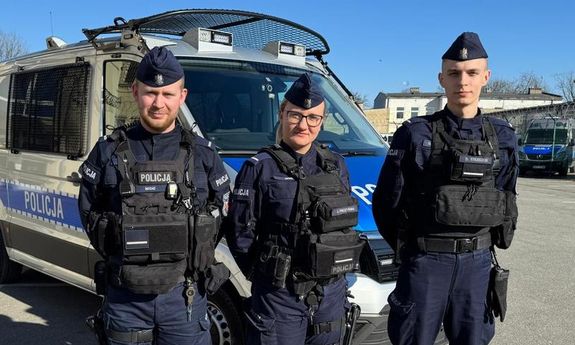 troje policjantów stoi przed radiowozem.