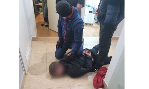 Zatrzymany mężczyzna leży na ziemi, przy nim kuca zatrzymujący go policjant. Obok stoi drugi policjant. Obaj funkcjonariusze są nieumundurowani.