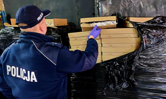 Policjant w mundurze otwierający pudełko z papierosami.
