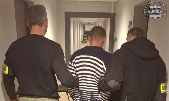 Dwaj nieumundurowani policjanci trzymają zatrzymanego mężczyznę.