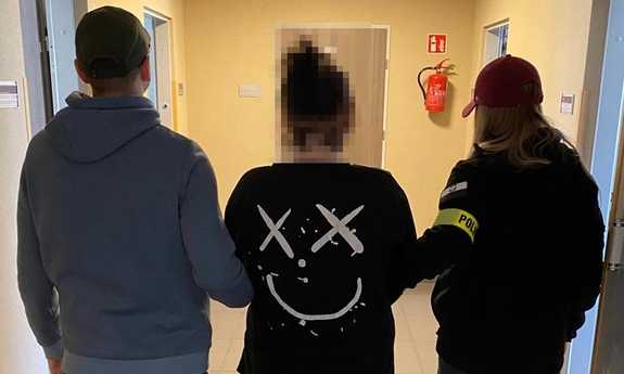Dwoje funkcjonariuszy prowadzi korytarzem zatrzymaną kobietę zakutą w kajdanki.
